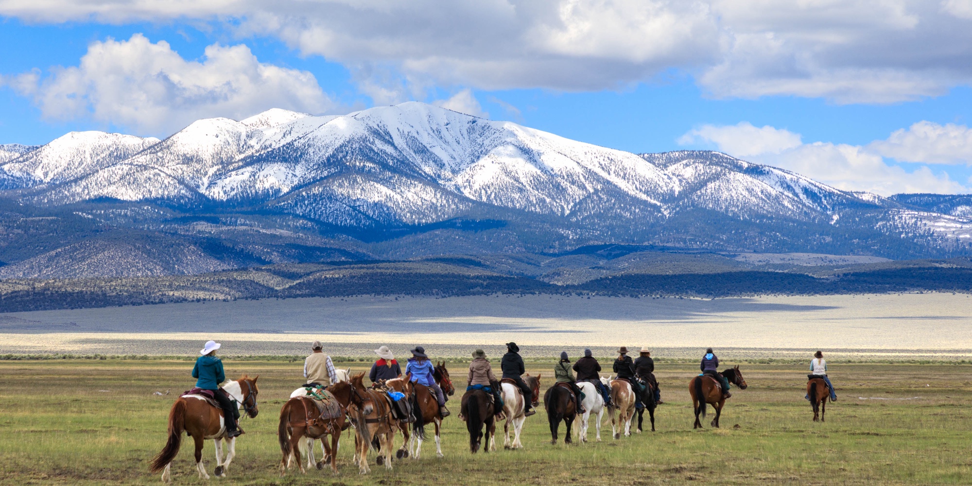 Riders on horseback below snow-covered peaks