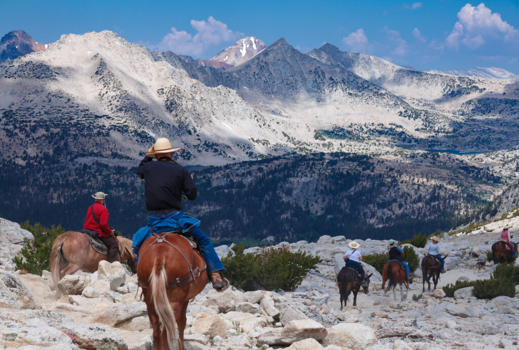 Riders on horseback below the snow-streaked peaks of the High Sierra